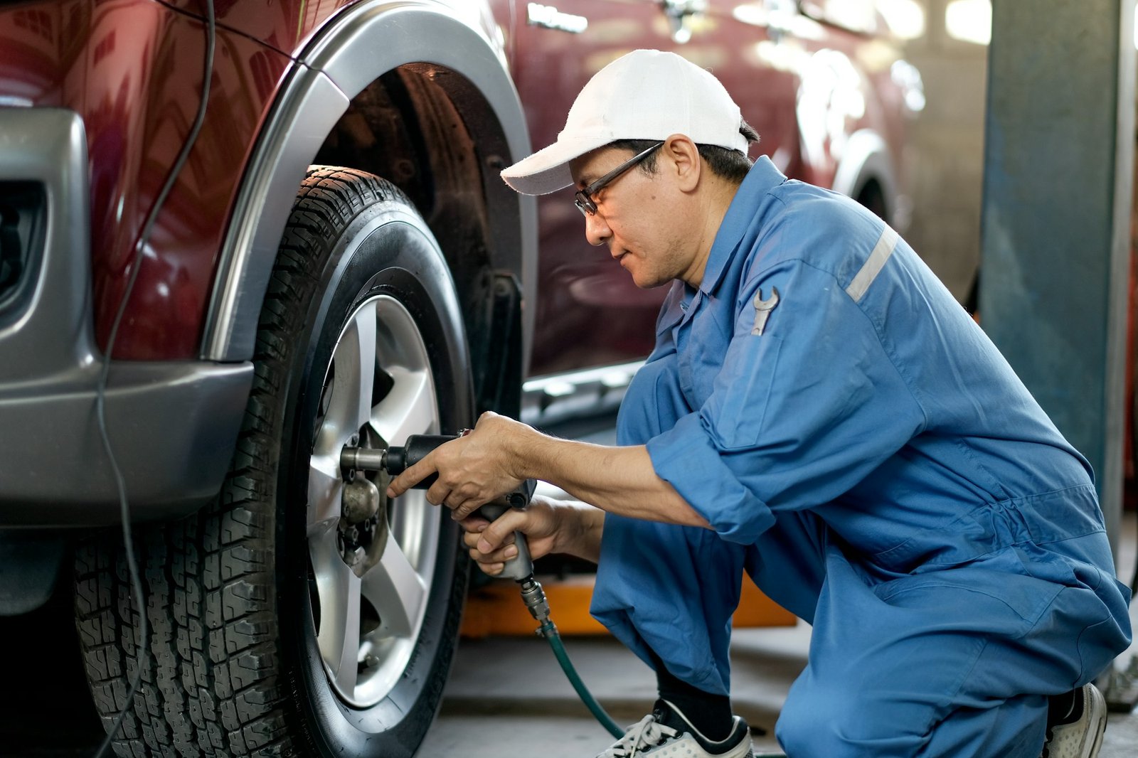 Asian automotive mechanic with white cap and blue uniform is working with replace